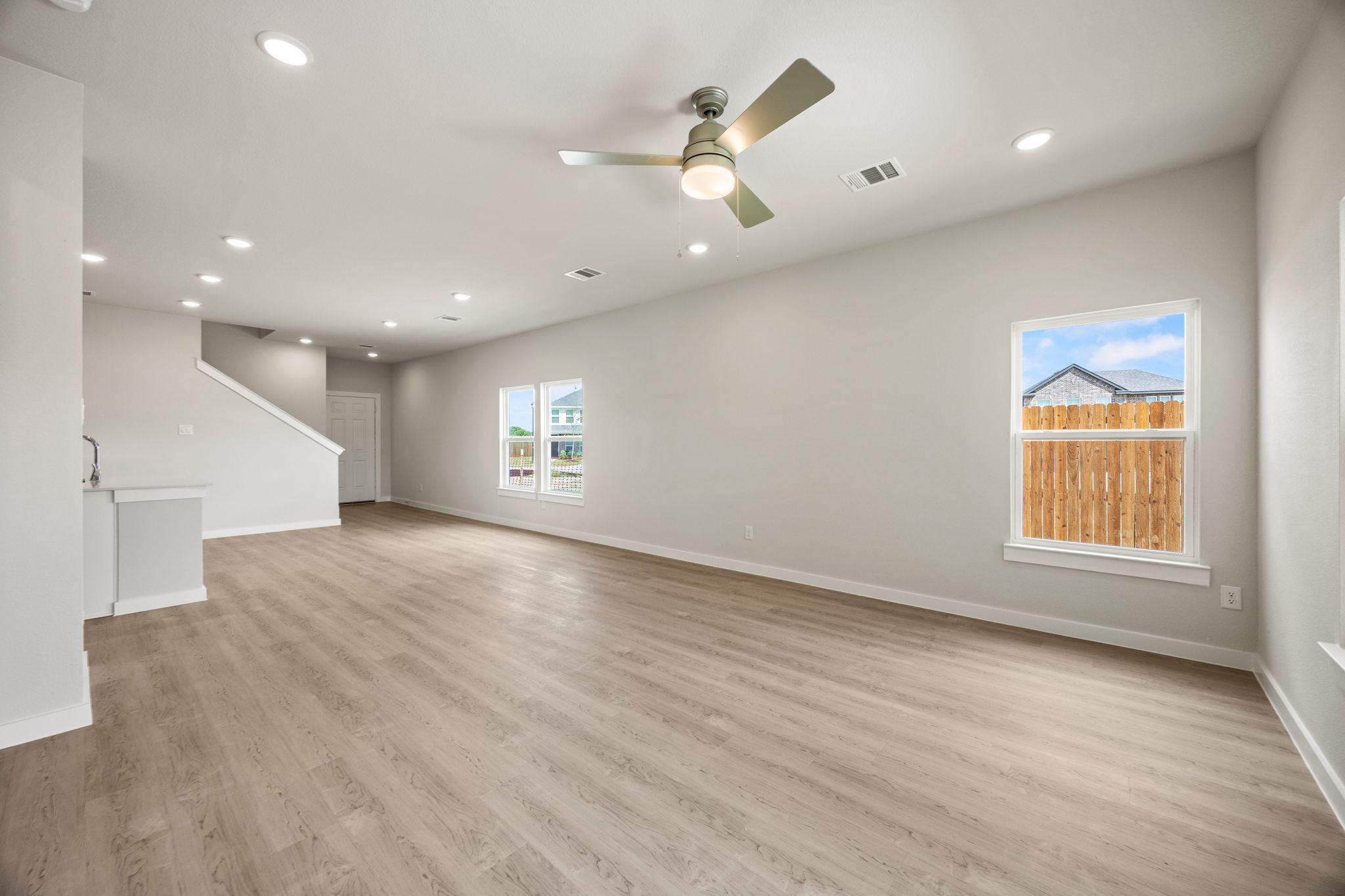 A large empty room with a ceiling fan and a wood floor.